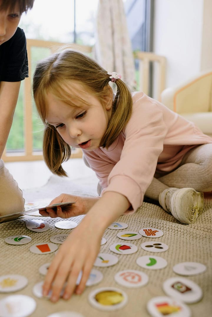 A young girl playing with educational cards on a rug, engaged in fun learning indoors.